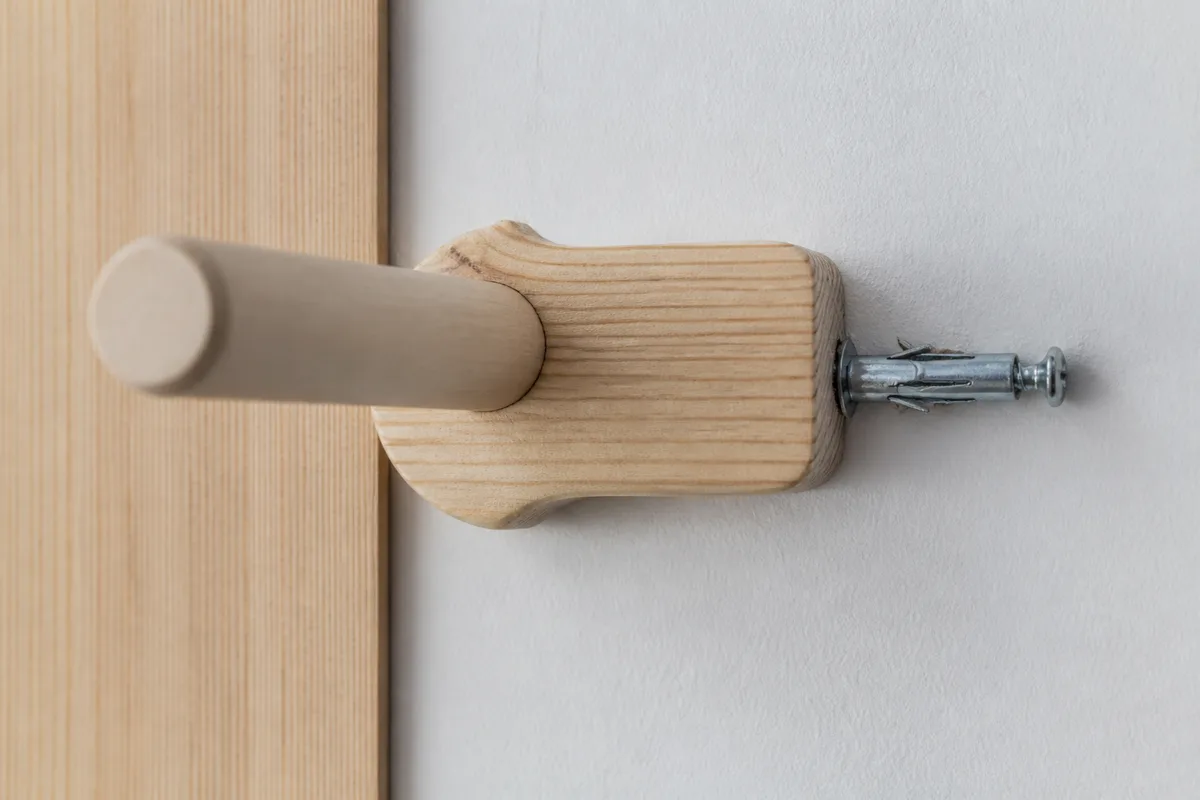 Détail d’une patère en bois clair fixée sur une cloison, cheville métallique visible avant recouvrement